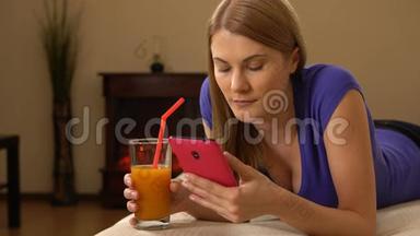 年轻漂亮迷人的女人躺在沙发上，喝着果汁，在电话上浏览。 00345